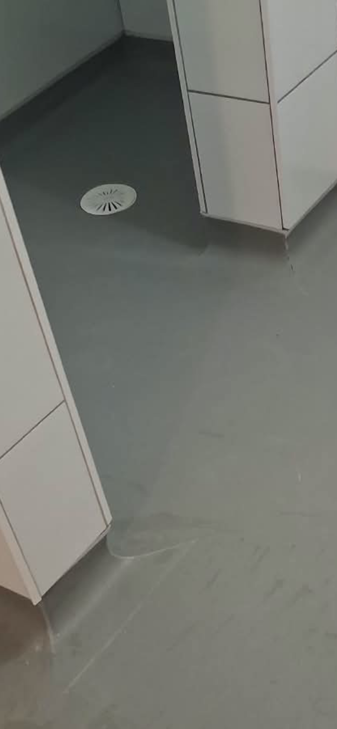 Grey safety flooring extending into the shower area around tiled partitions